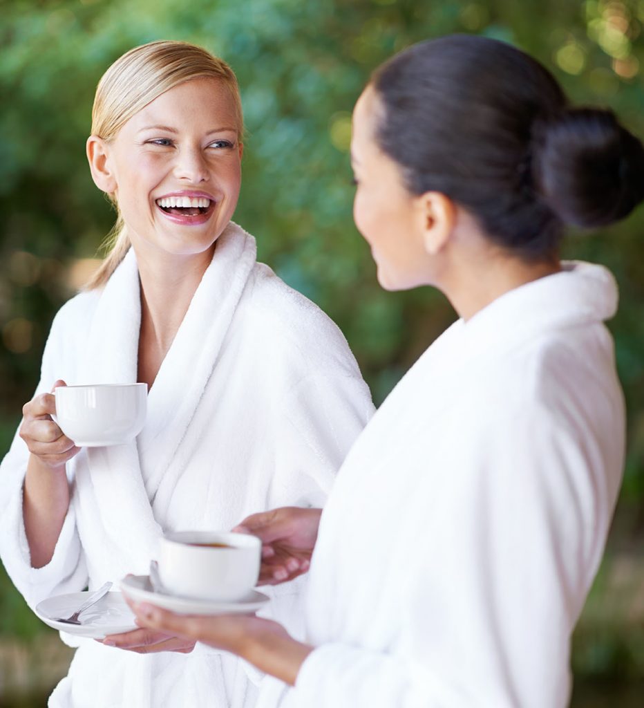Two young women having coffee in their bathrobes at the spa